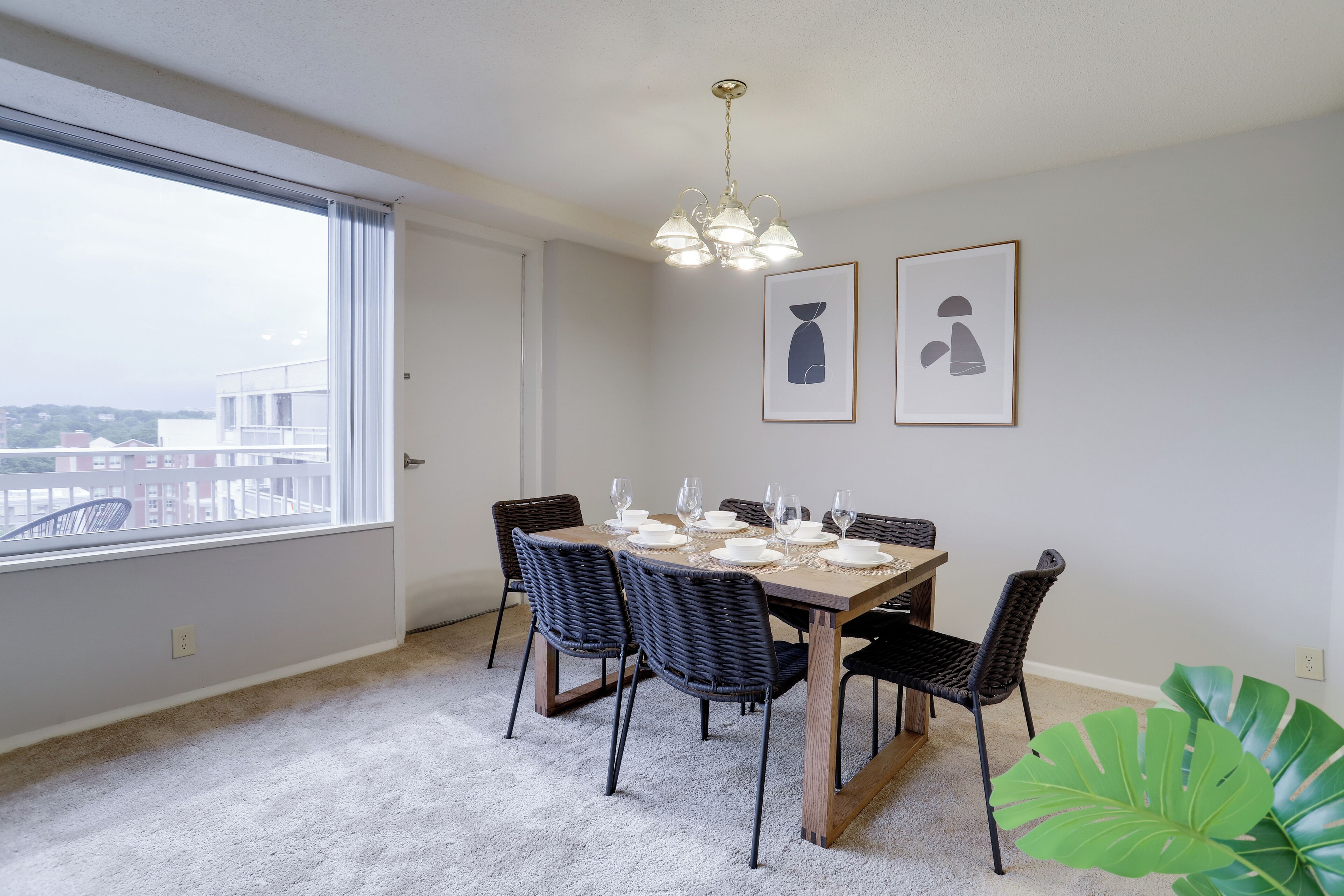 Een eetruimte met een tafel voor zes personen, zes stoelen, een kroonluchter en twee ingelijste foto’s aan de muur.