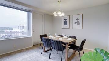 A dining area with a table set for six, six chairs, a chandelier, and two framed pictures on the wall.