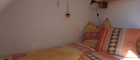 A bedroom with a bed, patterned bedding, a hanging light fixture, and a shelf with a picture.