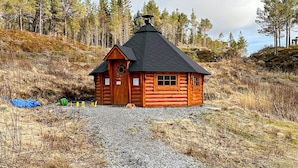 A log cabin with a steeply pitched roof and a chimney, surrounded by a gravel driveway and sparse vegetation. - 4 Person Holiday Home in Lysoysundet (Orland)