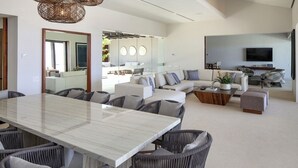 Ein modernes Wohnzimmer mit einem Esstisch aus Marmor, grau gepolsterten Sesseln, einem grauen Sofa und einem an der Wand befestigten Fernseher.