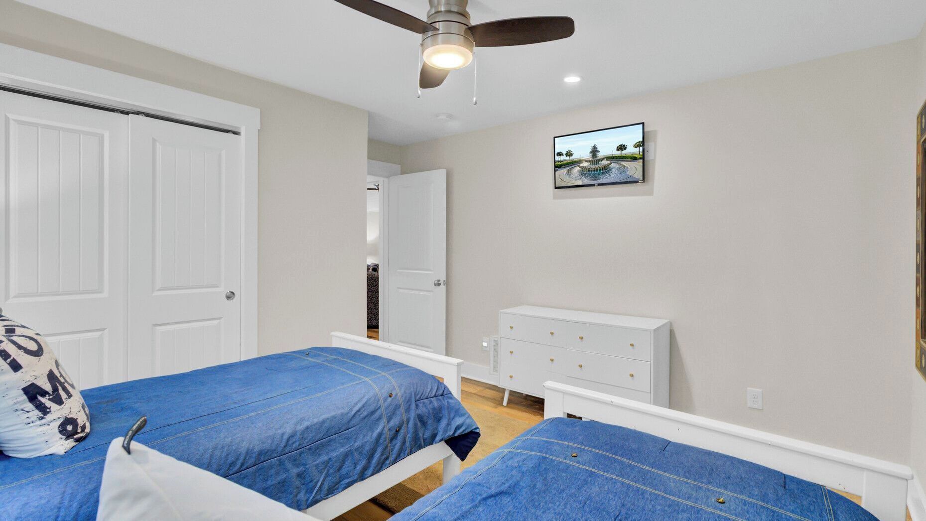 Une chambre avec deux lits, un ventilateur de plafond, une commode et un téléviseur fixé au mur.