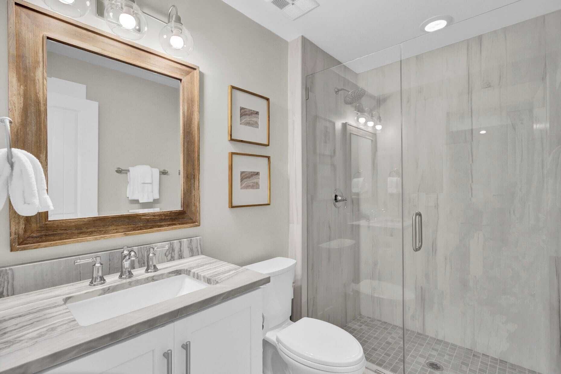 Un bagno moderno con un vanità in marmo, uno specchio grande e una cabina doccia in vetro.