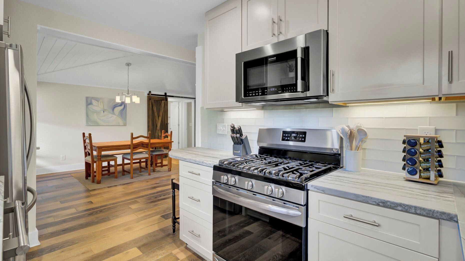 A modern kitchen with a gas stove, oven, microwave, and white cabinetry.