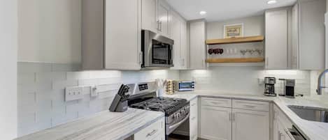 A modern kitchen with white cabinetry, a built-in microwave, a gas stove, and a coffee maker.