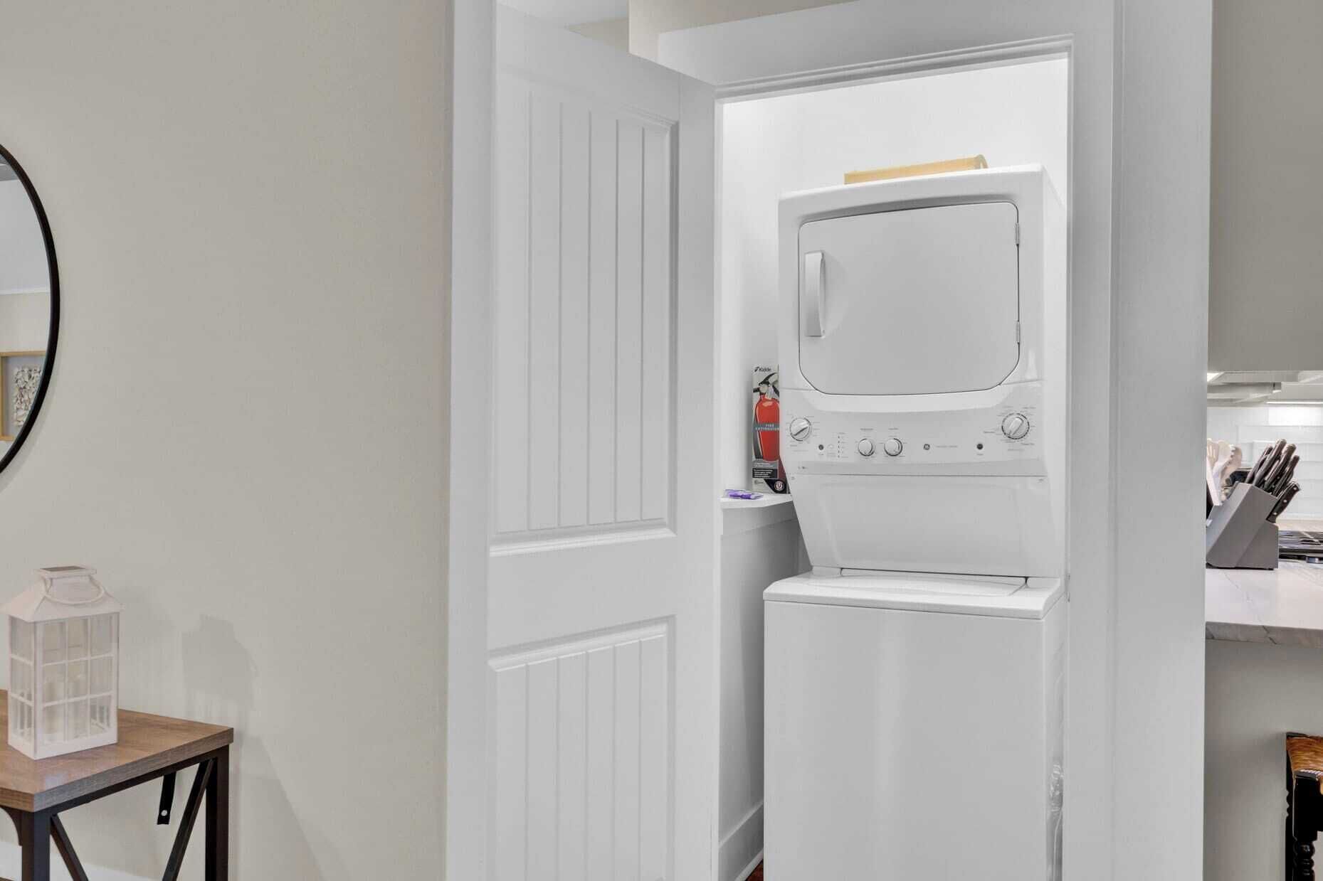 A compact, white laundry room with a built-in washer and dryer, a small table with a lantern, and a knife block on the right.