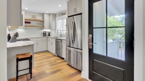 A modern kitchen with white cabinets, stainless steel appliances, and a wooden floor.