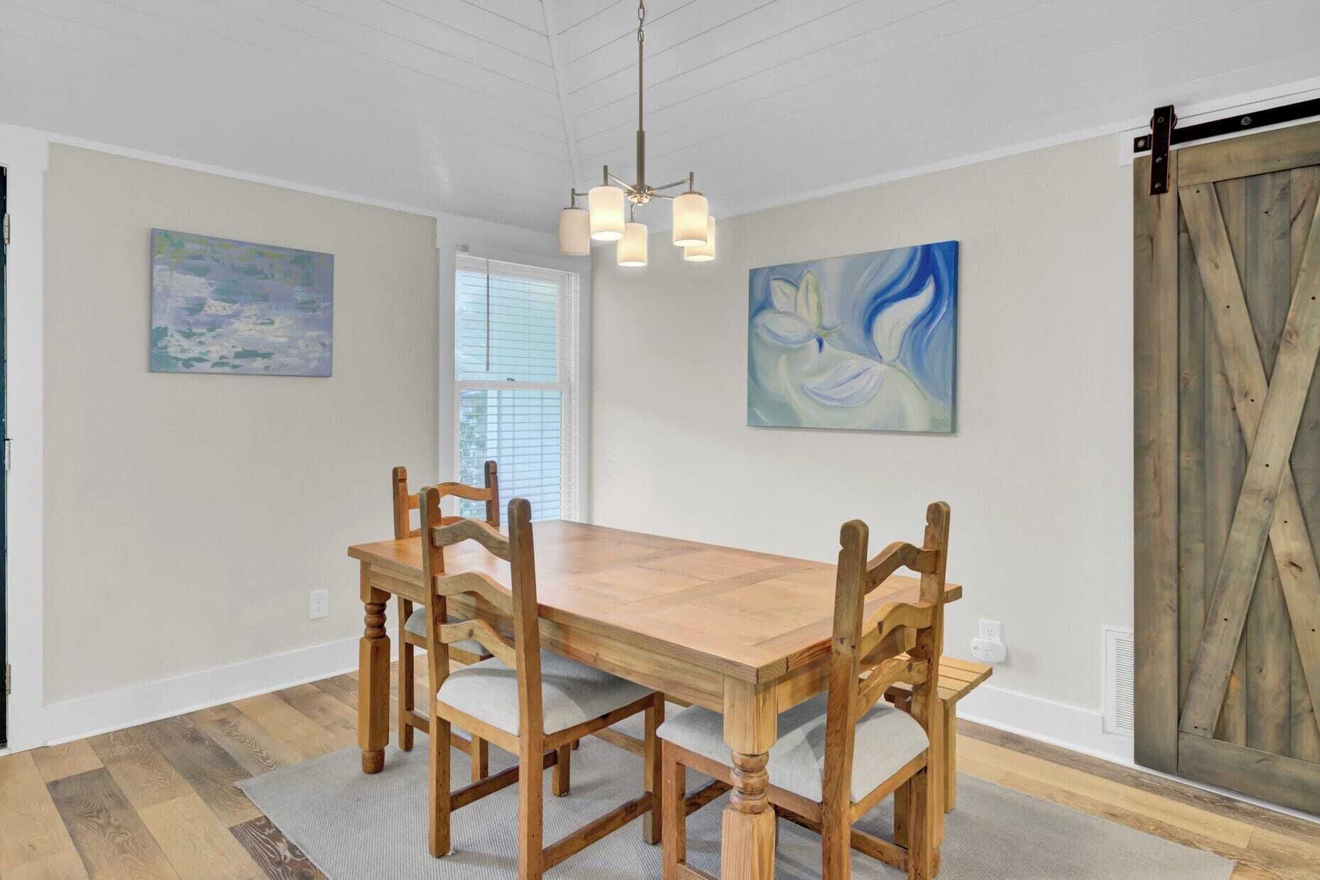 Een eetkamer met een houten tafel en stoelen, een kroonluchter en twee schilderijen aan de wand.