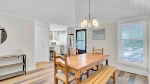 A dining area with a wooden table and chairs, a hanging light fixture, and a view of the kitchen and dining room through an open door. - 10 Sandcrab Court by Avantstay Beautiful Home w/ Deck, Walk to the Beach (Isle of Palms)