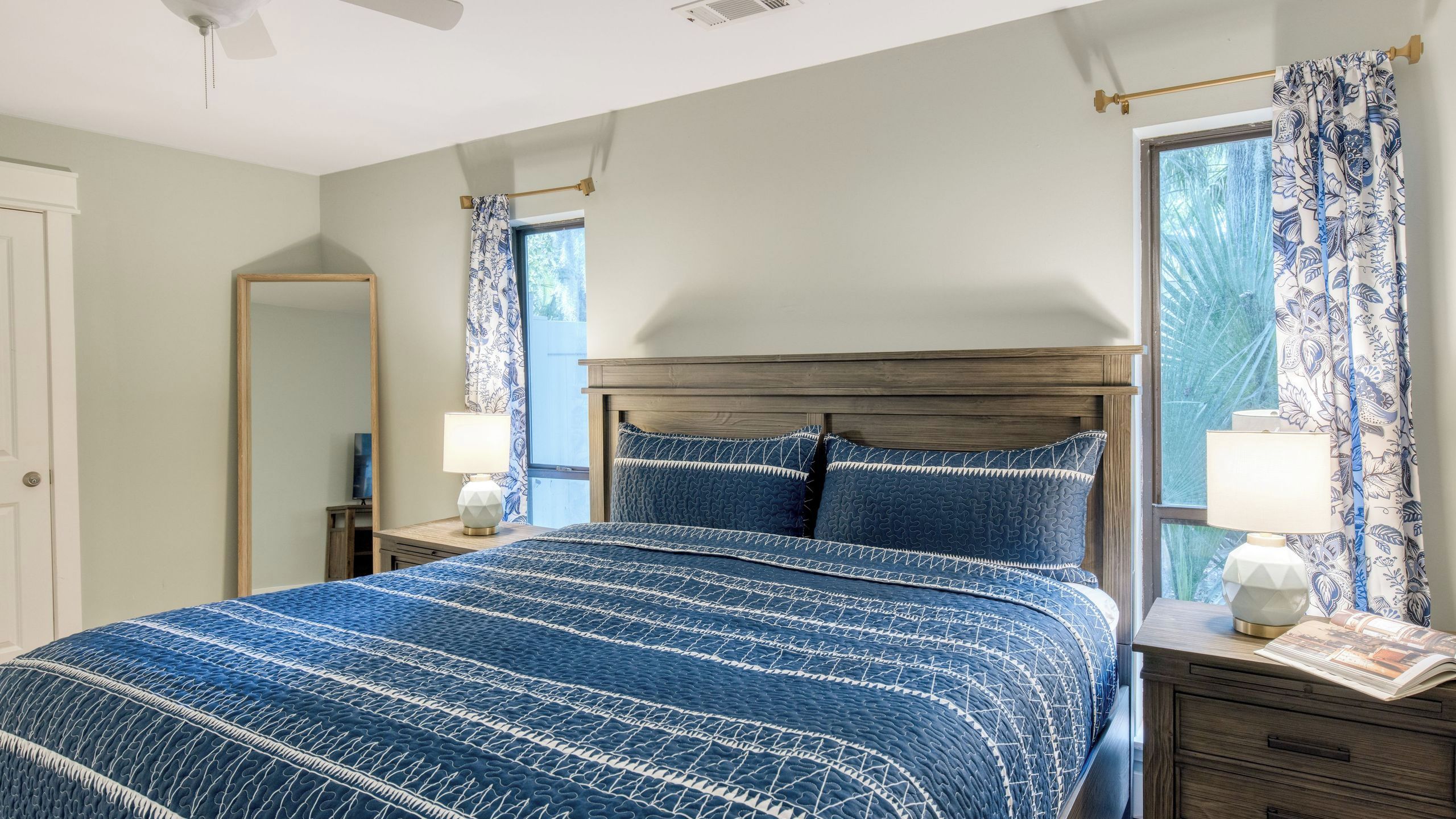 Un dormitorio con cama, dos mesitas de noche, un espejo y una ventana con cortinas.
