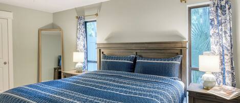 Un dormitorio con cama, dos mesitas de noche, un espejo y una ventana con cortinas.