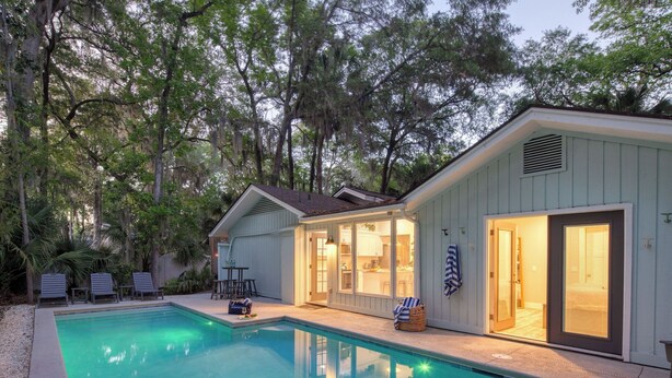 A poolside area with a pool, lounge chairs, and a building with a sliding glass door. - Hilton Hideaway by Avantstay Private Pool, Walk to Beach (Hilton Head Island)