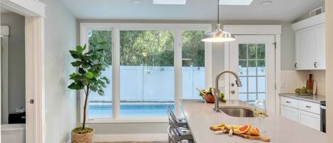 A modern kitchen with a large island, a built-in sink, and a view of a backyard with a pool.