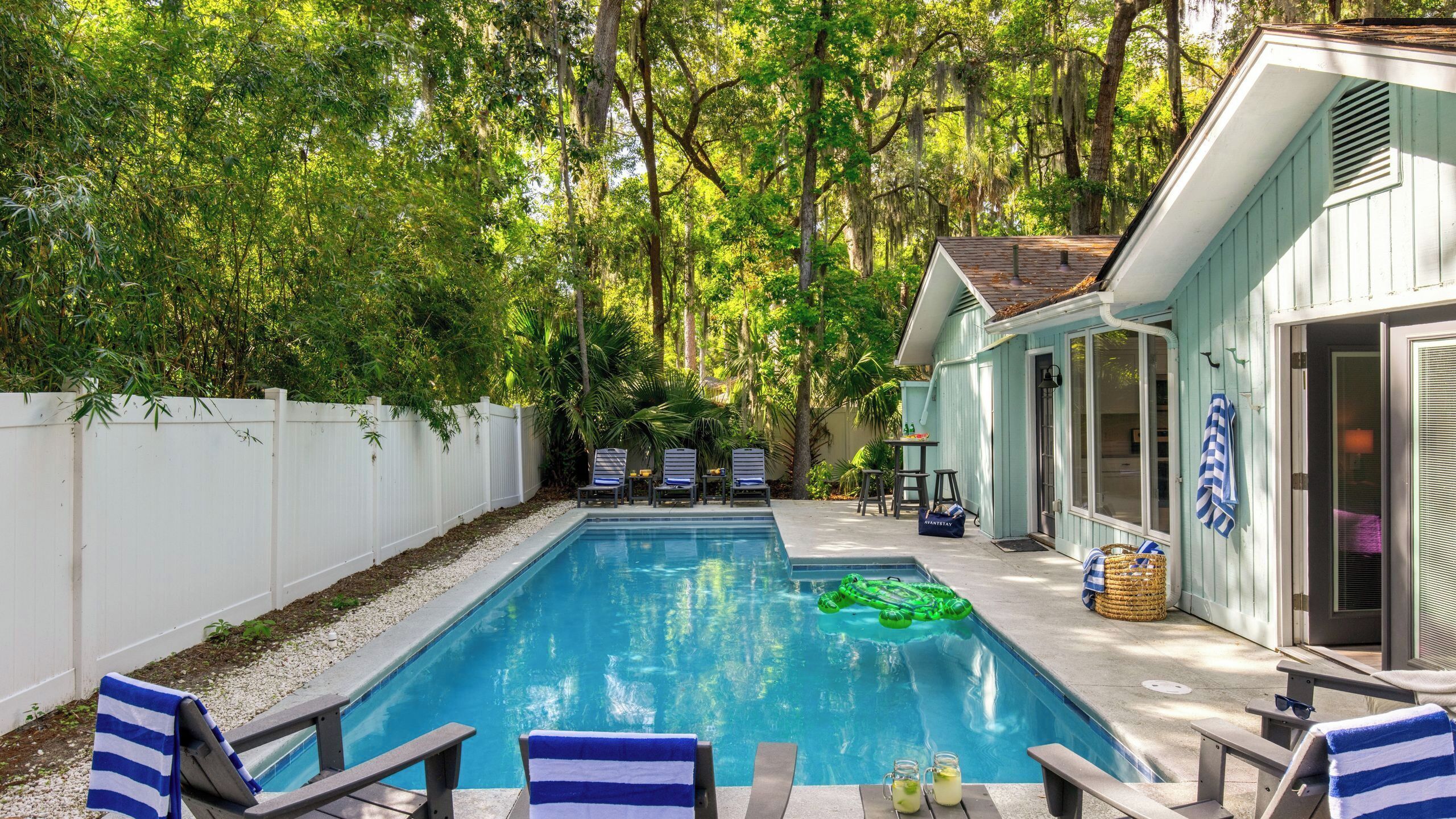 A backyard with a swimming pool, lounge chairs, and a house.