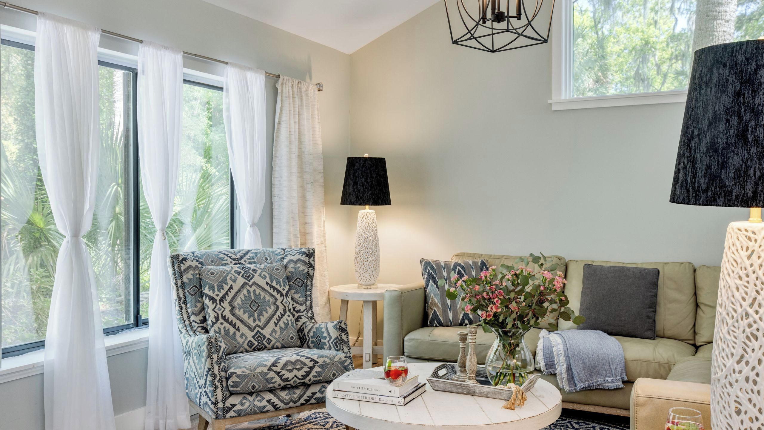 Un salon comprenant un fauteuil à motifs, une table basse ronde avec des livres et un vase, un canapé avec des coussins et une lampe sur une table d’appoint.
