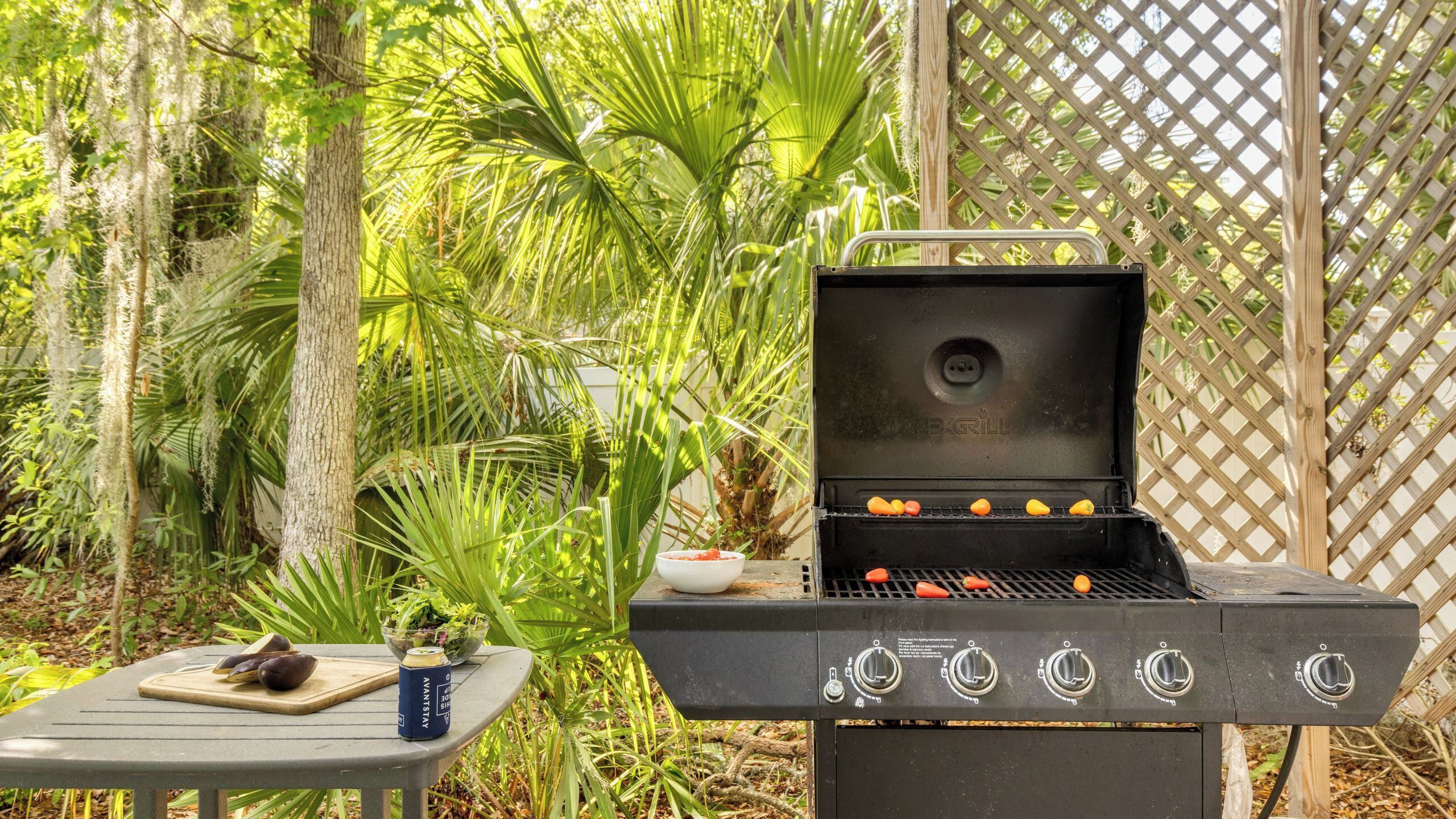 Una parrilla con varios quemadores, una tabla de cortar con verduras y una lata de cerveza sobre una mesa.