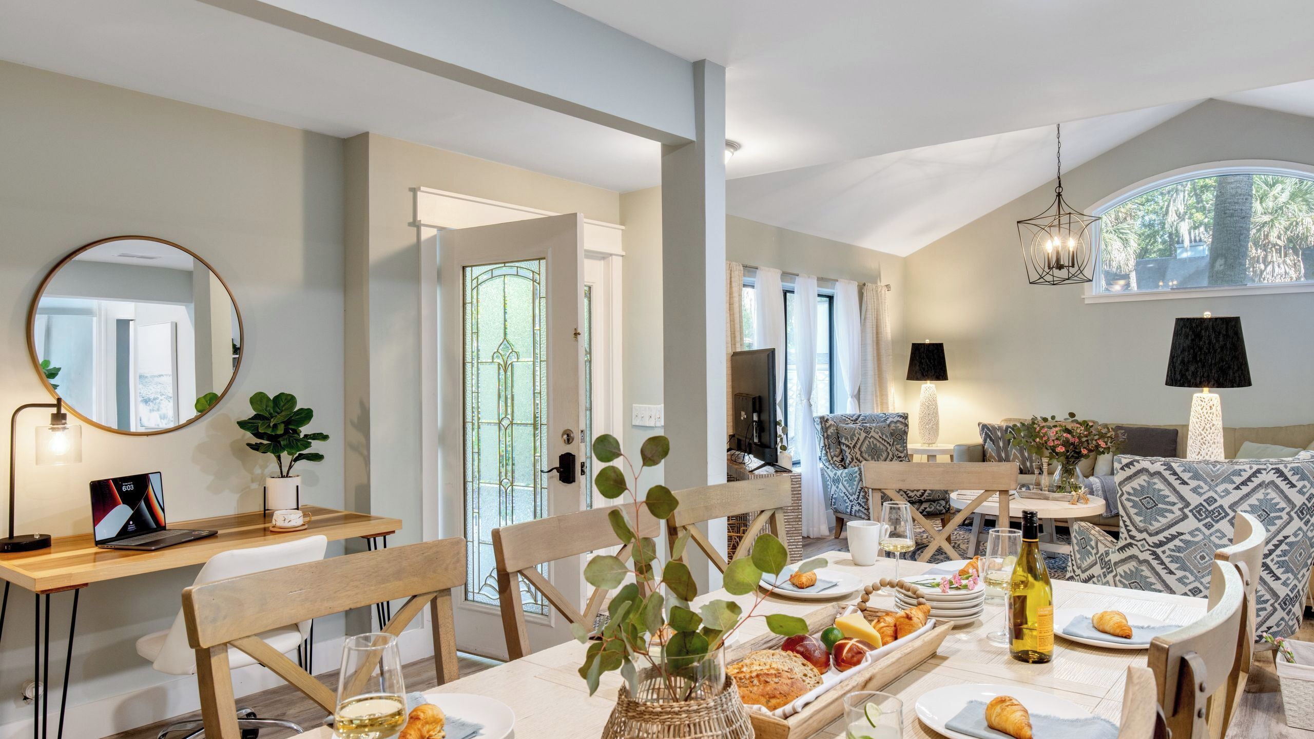 A dining area with a table set for a meal, a laptop on a desk, and a mirror on the wall.
