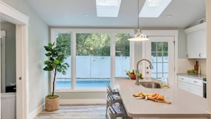 Une cuisine moderne dotée d’un grand îlot central, d’un évier intégré et donnant sur une piscine située dans le jardin.