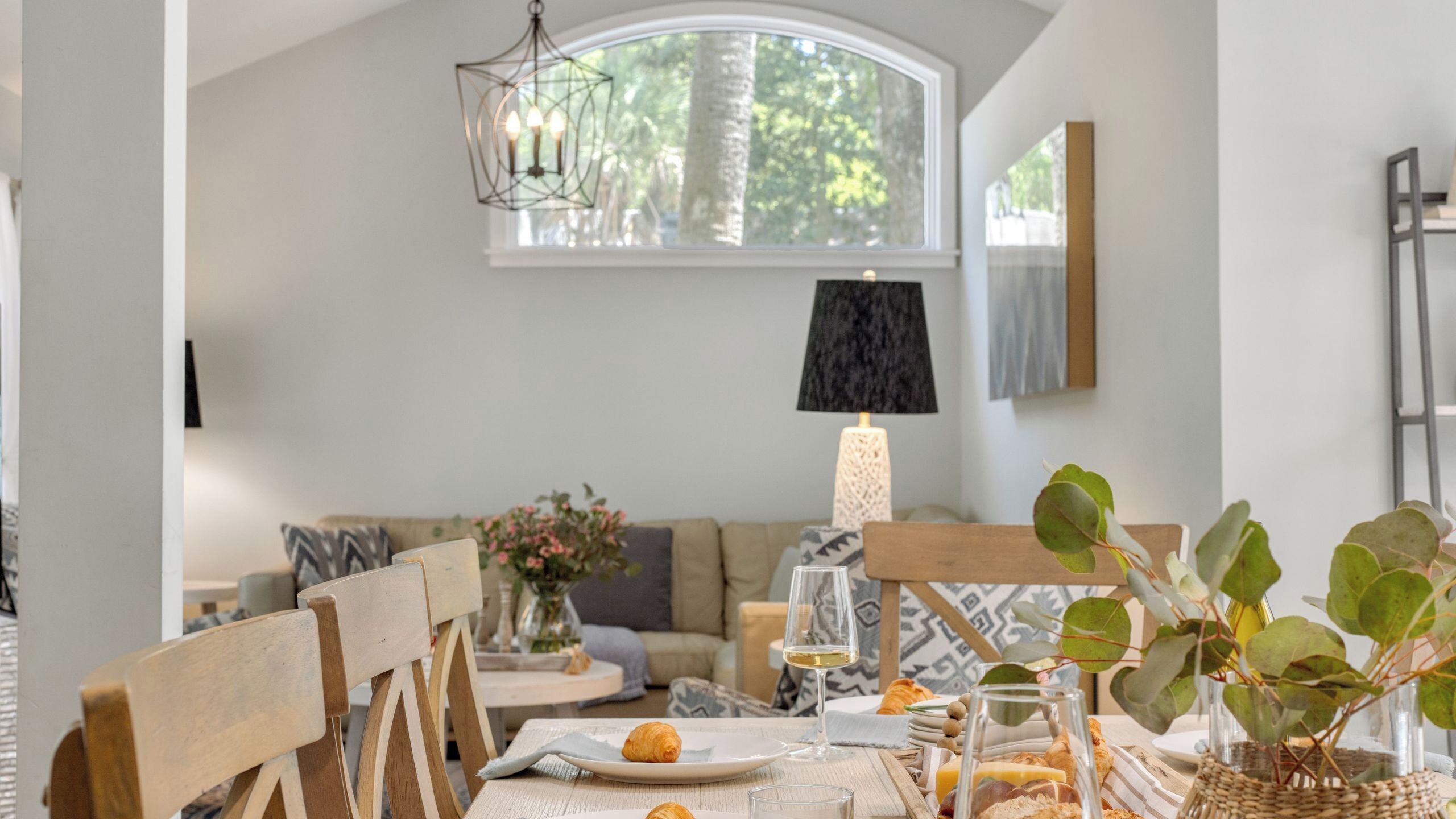 Zona pranzo con tavolo apparecchiato per due, un lampadario, una lampada e vista sull'esterno.