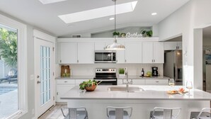 A modern kitchen with white cabinetry, a central island, a built-in oven, a microwave, and a refrigerator. - Hilton Hideaway by Avantstay Private Pool, Walk to Beach (Hilton Head Island)