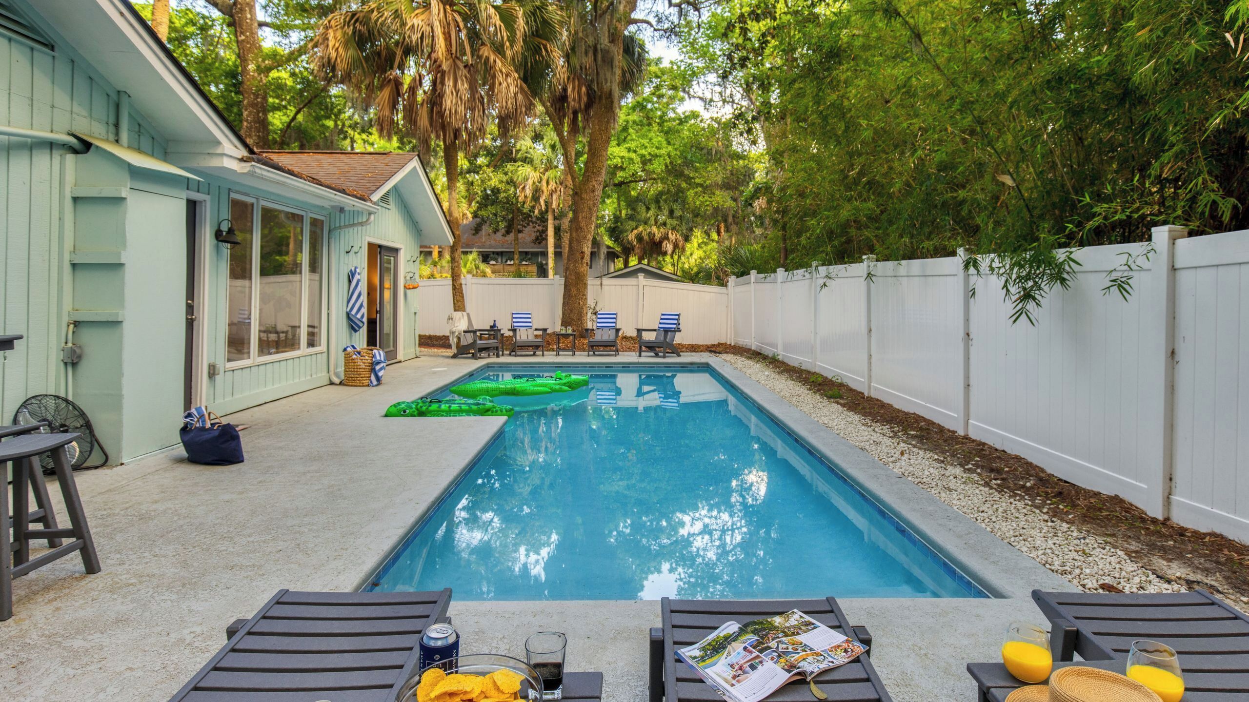 Un jardin avec une piscine, des chaises longues et une clôture blanche.