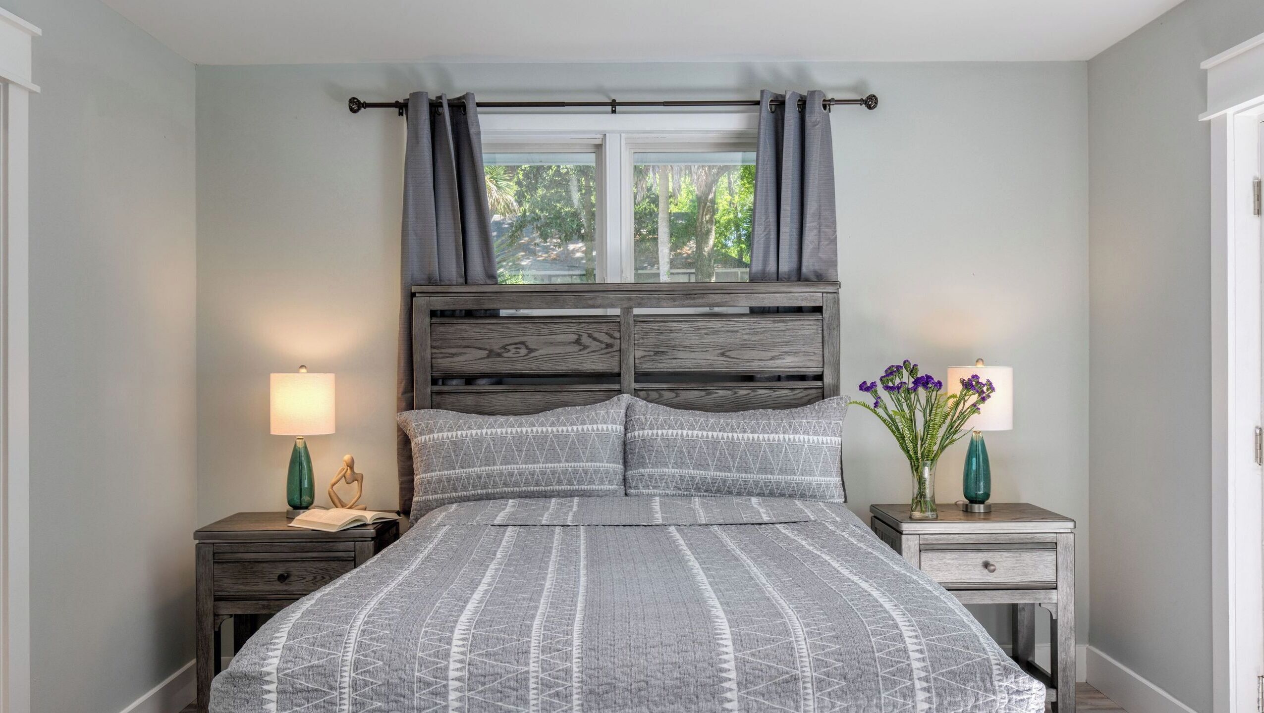 Une chambre à coucher comprenant un lit, deux tables de chevet, une fenêtre avec des rideaux et une petite table de nuit avec une lampe.