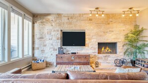 A living room with a stone wall, a flat-screen TV, a fireplace, leather sofas, and a large window. - Sunvail by Avantstay 10min Walk to Ski Lifts! (Vail)