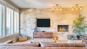 A living room with a stone wall, a flat-screen TV, a fireplace, leather sofas, and a large window. - Sunvail by Avantstay 10min Walk to Ski Lifts! (Vail)