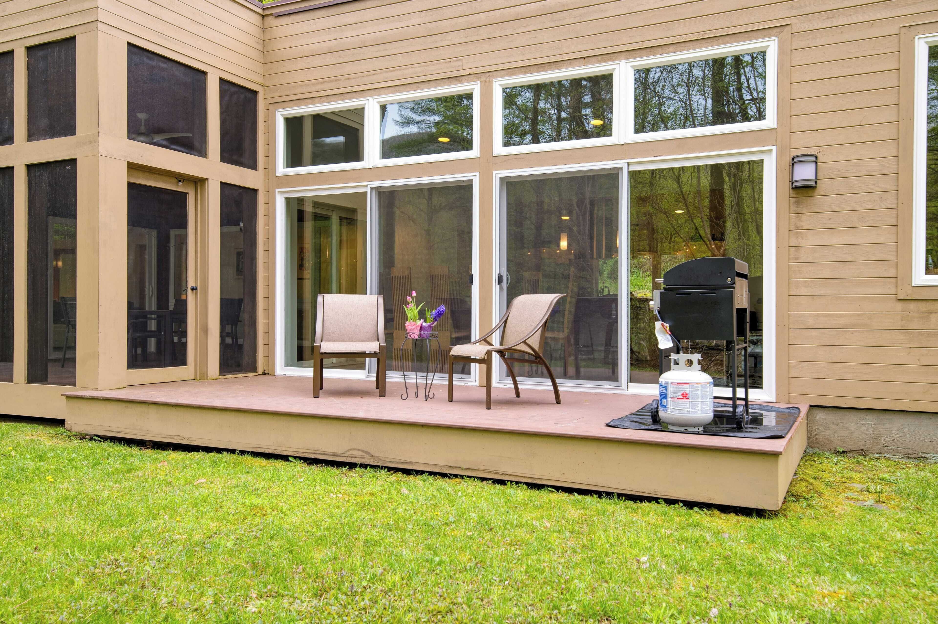 Een overdekt terras met twee stoelen, een barbecue en een propaantank.