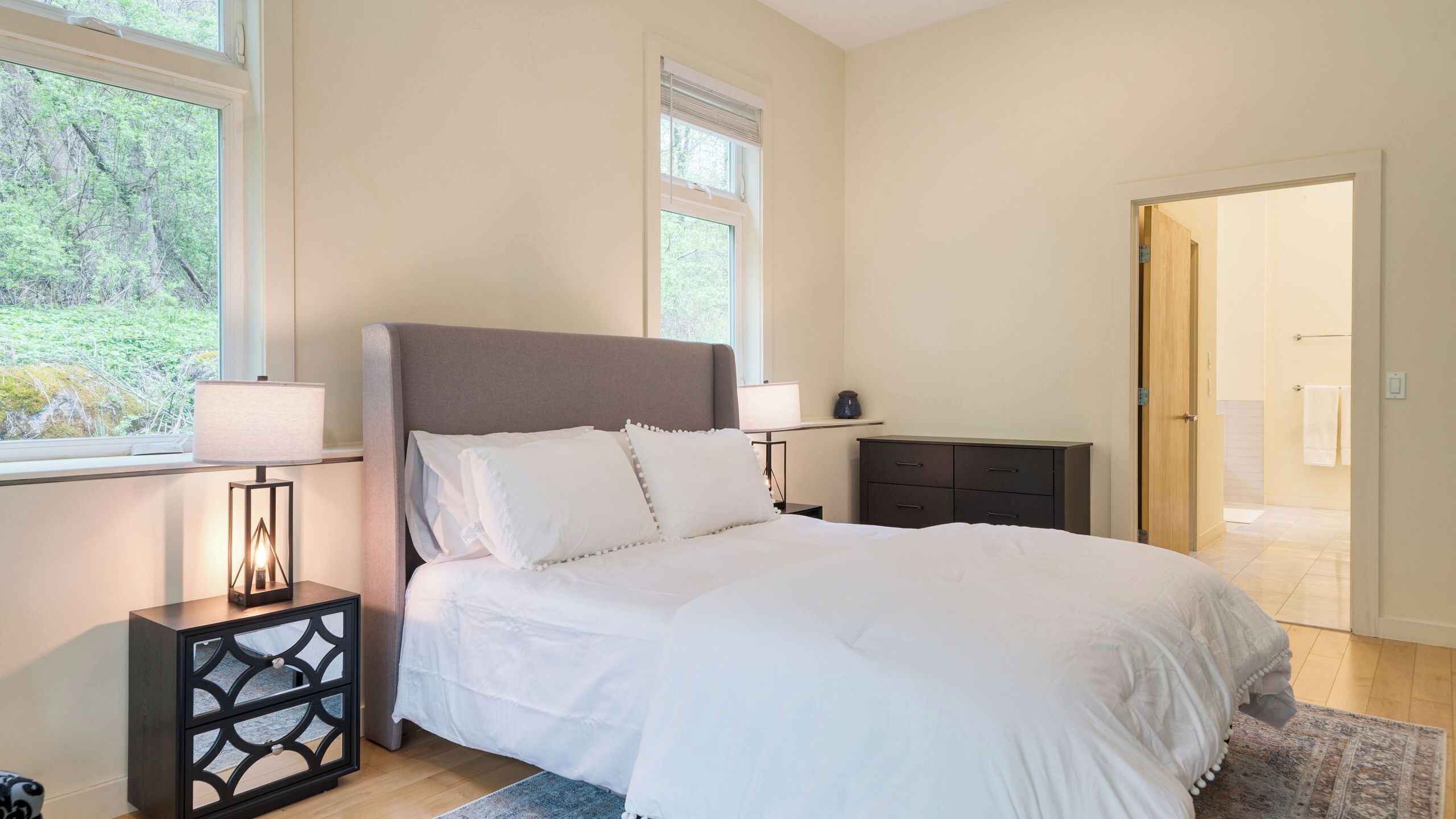A bedroom with a bed, bedside lamps, a dresser, and a window with a view of trees.