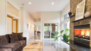 A modern living room with a fireplace, a sofa, a coffee table, and a large window. - Secluded + Modern Enclosed Patio, Forest Views Woodland Zen by Avantstay (Housatonic)