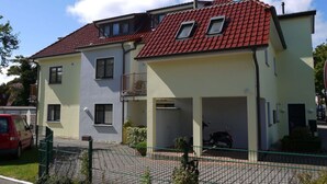 A two-story residential building with a red-tiled roof, a covered garage, and a fenced yard. - 1 in House Weser 1 Comfortable Vacation Home (Cuxhaven)
