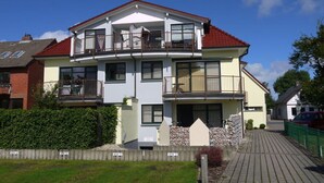 A two-story residential building with a balcony on the upper floor, a small front porch, and a paved driveway. - 1 in House Weser 1 Comfortable Vacation Home (Cuxhaven)