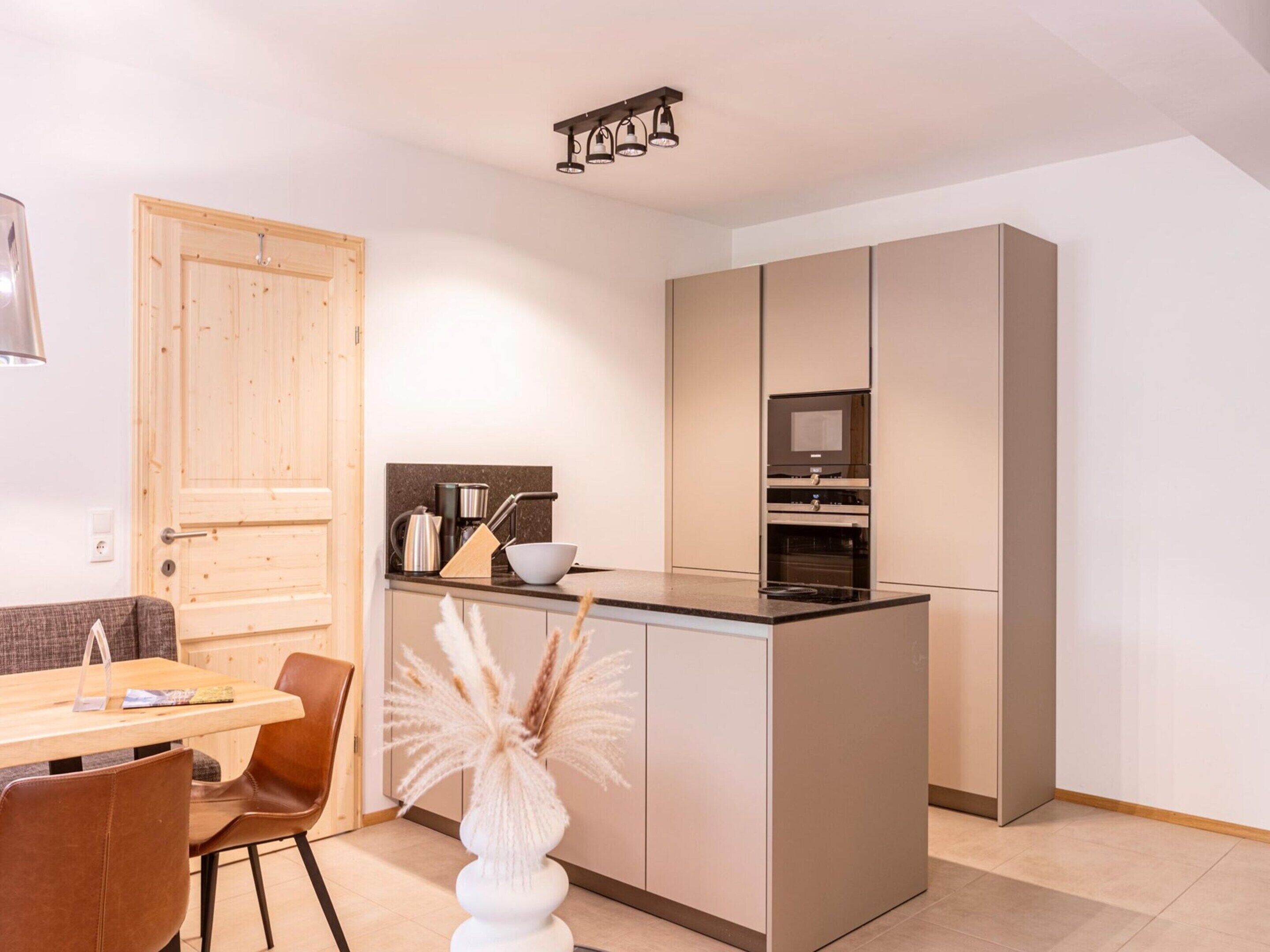 Una cocina compacta con una isla central, una puerta de madera y un comedor con mesa y sillas.