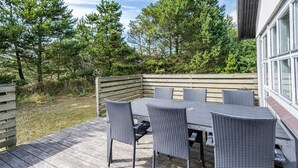 An outdoor patio with a table and chairs, surrounded by trees and a wooden deck. - 4 Person Holiday Home in Blavand (Blavand)