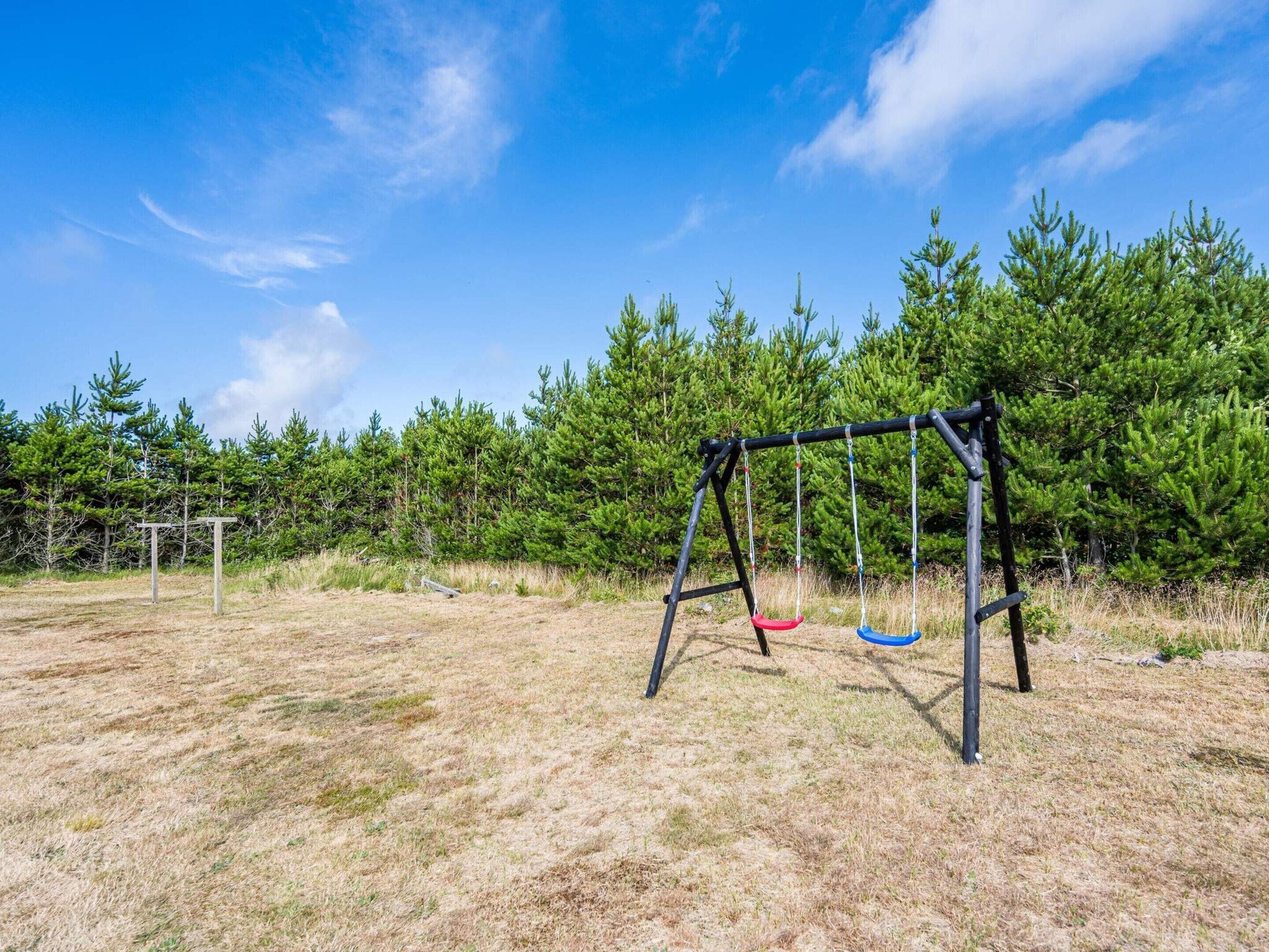 A swing set in a grassy field with trees in the background.