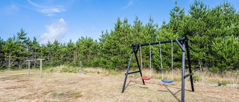 A swing set in a grassy field with trees in the background.
