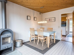 A dining area with a wood-burning stove, a table with chairs, framed pictures on the wall, and a hanging light fixture.