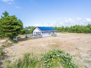 A single-story house with a blue roof, a fenced yard, and a large tree to the left. - 4 Person Holiday Home in Blavand (Blavand)