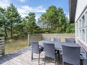 An outdoor patio with a table and chairs, surrounded by trees and a wooden deck. - 4 Person Holiday Home in Blavand (Blavand)