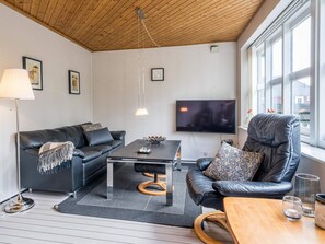 A modern living room with a leather sofa, a coffee table, a wooden chair, a TV, and a large window. - 4 Person Holiday Home in Blavand (Blavand)