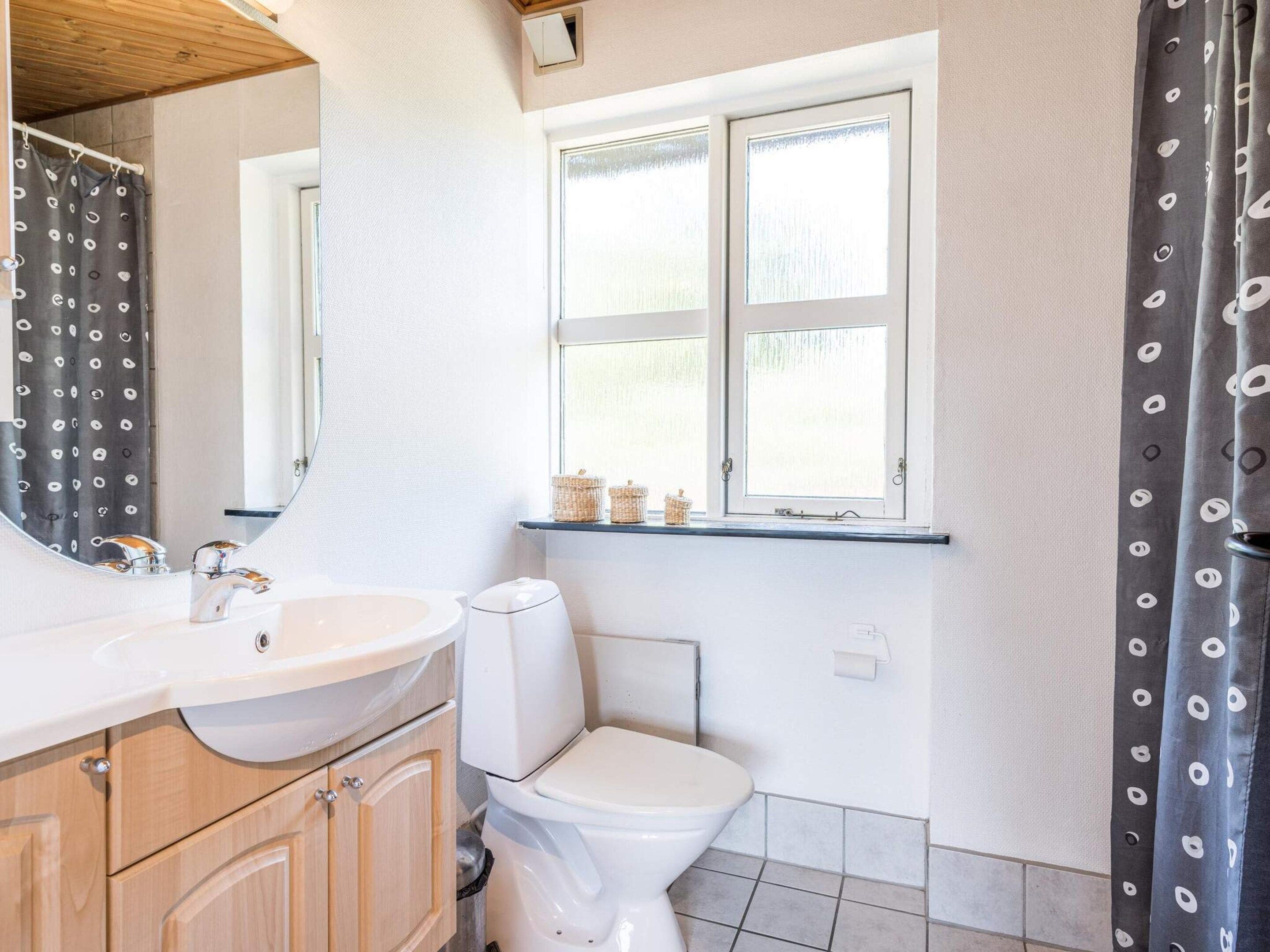 A bathroom with a sink, mirror, toilet, and window with baskets on the sill.