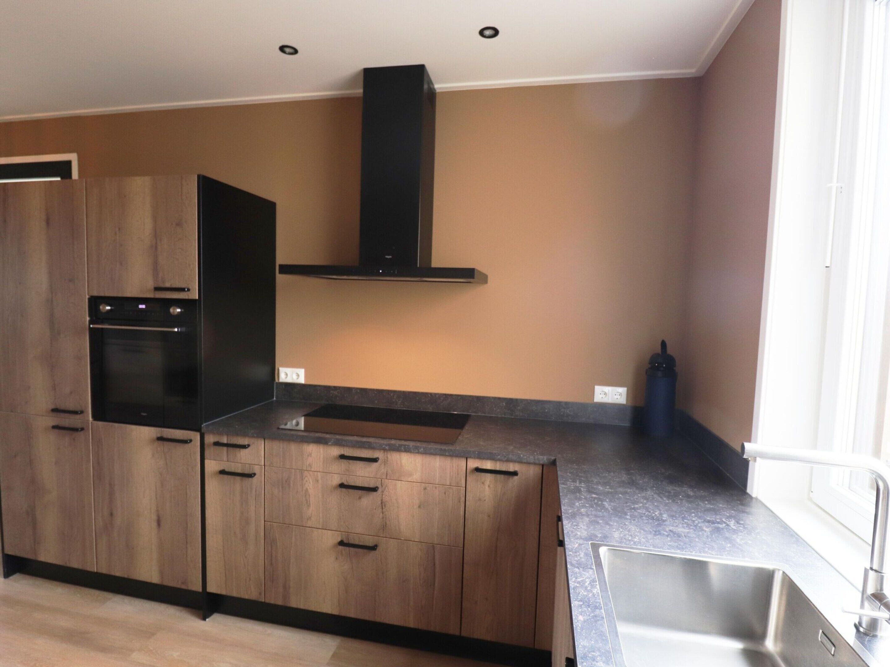 A modern kitchen with wooden cabinets, a built-in oven, a stainless steel sink, and a black range hood.