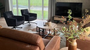 A modern living room with a leather sofa, two black armchairs, a coffee table, and a TV against a brick wall.