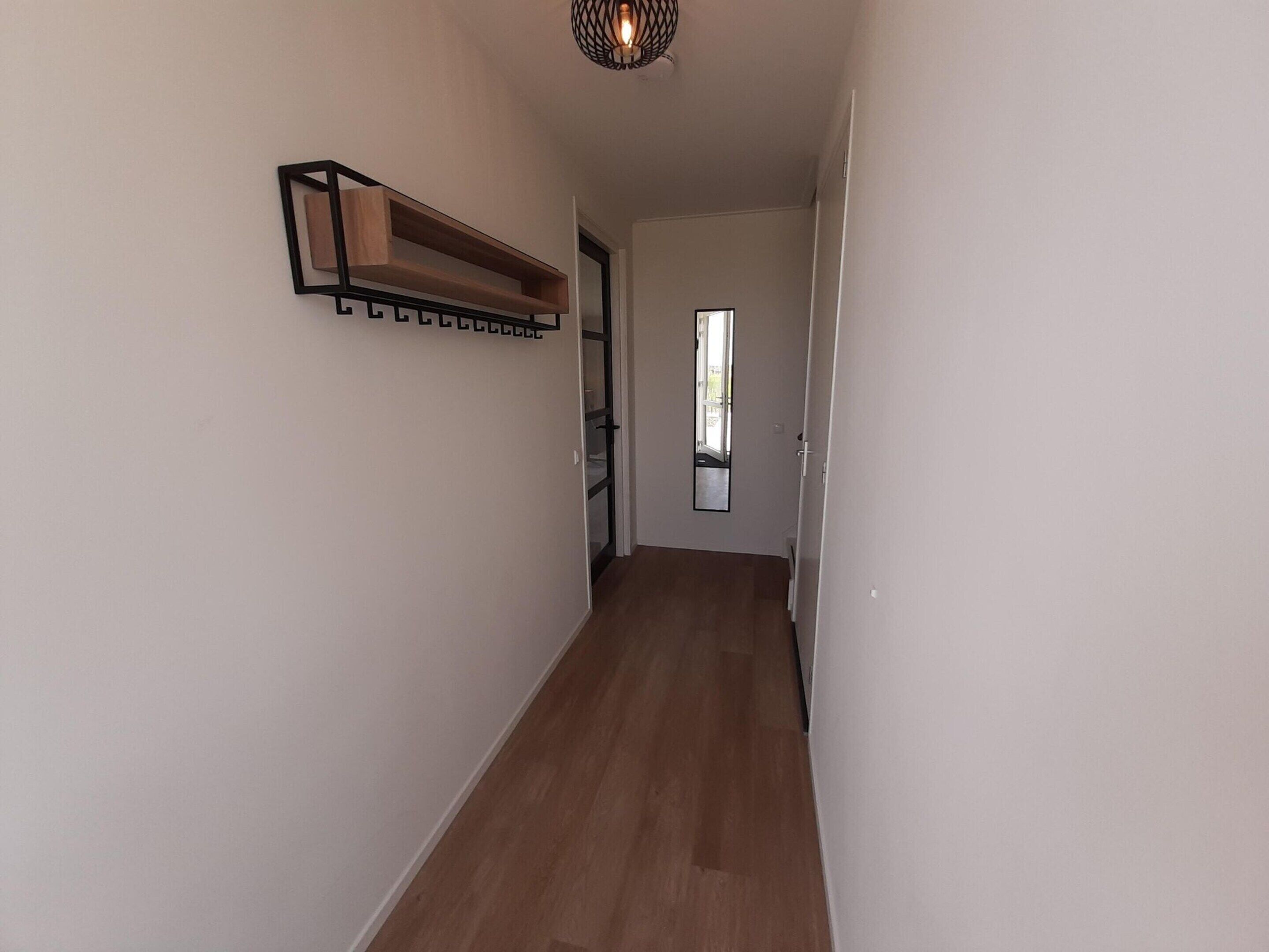 A narrow hallway with wooden flooring and a built-in shelf unit on the left wall.