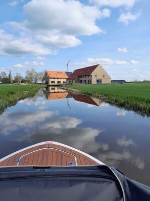 A calm river reflecting buildings, including a large structure with a red roof and a smaller building with a brown roof. - Lovely Villa on the Frisian Water (Leons)
