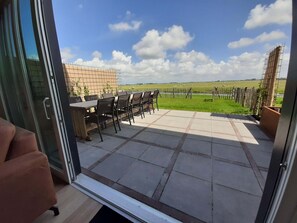 Une terrasse ouverte avec une table et des chaises, un mur en briques et une vue sur un champ verdoyant.