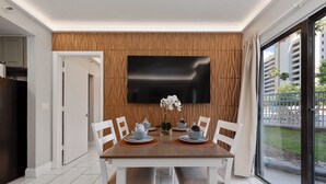 Un espace repas moderne avec un mur recouvert de panneaux en bois, un téléviseur à écran plat et une vue sur l’extérieur.