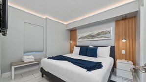 Une chambre à coucher moderne avec un grand lit, un banc, une table de chevet et un téléviseur fixé au mur.