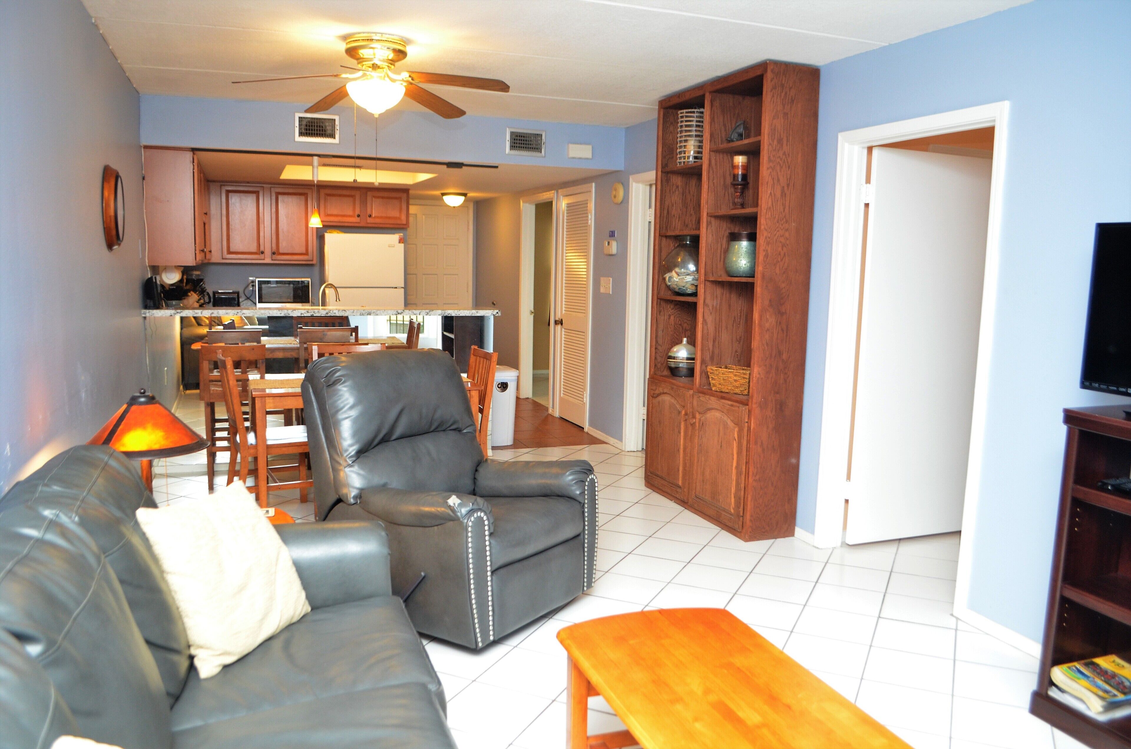 A living room with a leather sofa, a wooden coffee table, and a television on a stand. - Island Oasis Surfside 208 (South Padre Island)